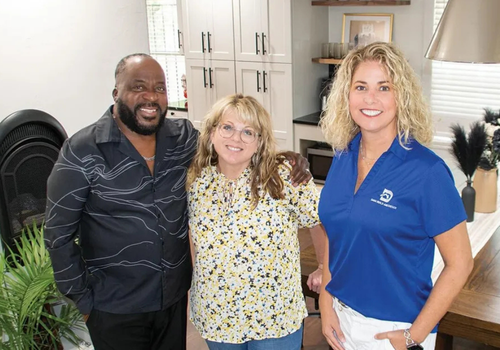 Three adults smiling inside a modern kitchen with white cabinets