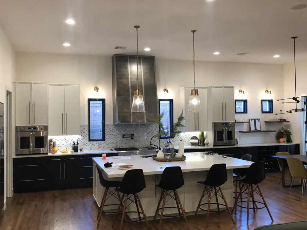 Spacious kitchen with large white island, black lower cabinets, white upper cabinets, pendant lighting, and hardwood floors