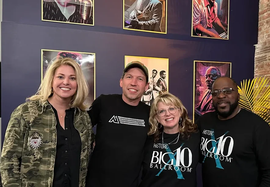 Four adults smiling indoors with framed music-themed artwork on the wall
