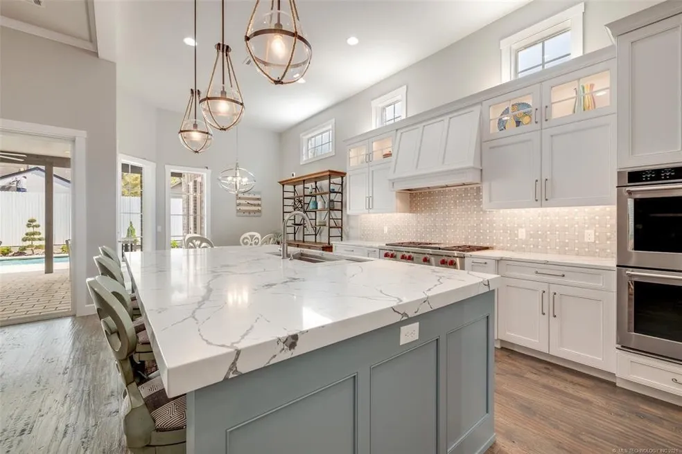 Bright kitchen with large marble island, white cabinetry, and pendant lighting