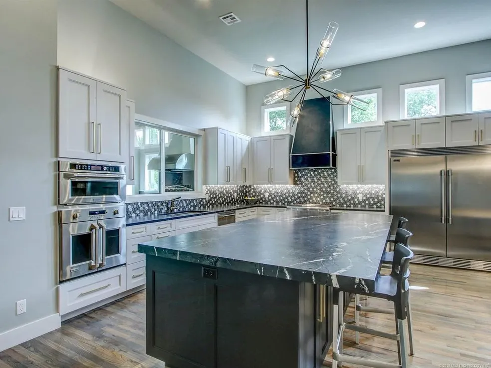 Spacious modern kitchen with large dark marble island, white cabinets, stainless steel appliances, and patterned backsplash
