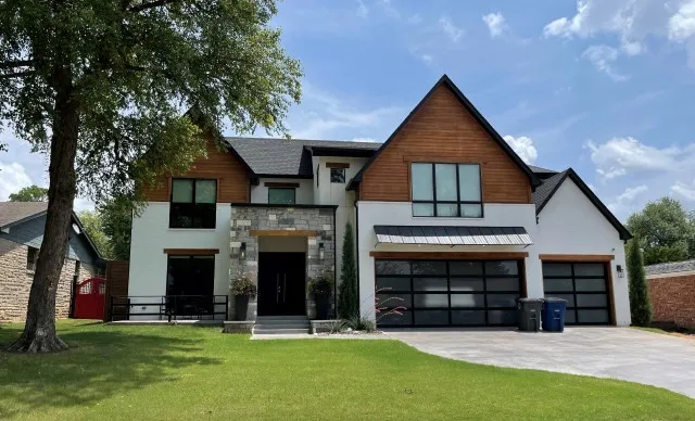 Front view of a modern two-story house with mixed wood, stone, and white siding and a three-car garage