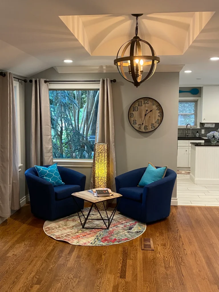 Two blue armchairs with blue pillows around a small wooden table on a round multicolor rug in sitting area