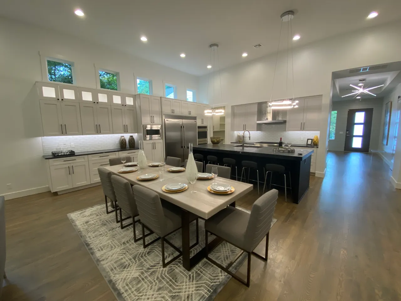 Spacious kitchen with white cabinets, black island, wood dining table, grey chairs, and pendant lights