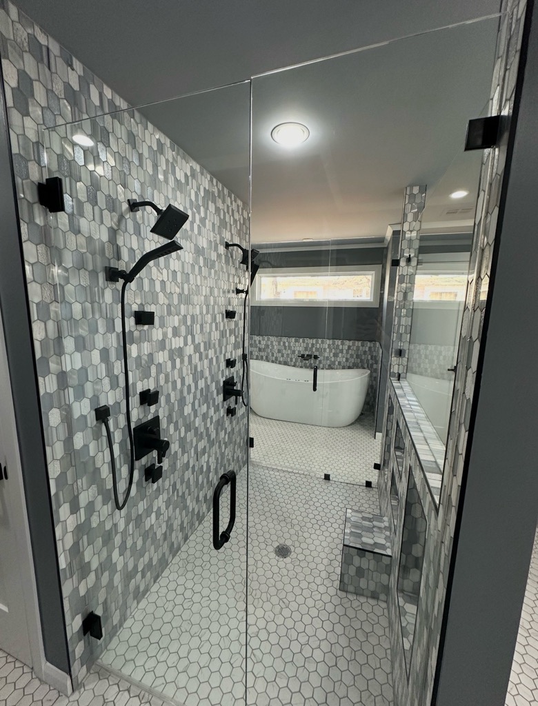 Bathroom shower with hexagonal gray and white mosaic tile and black fixtures, glass enclosure