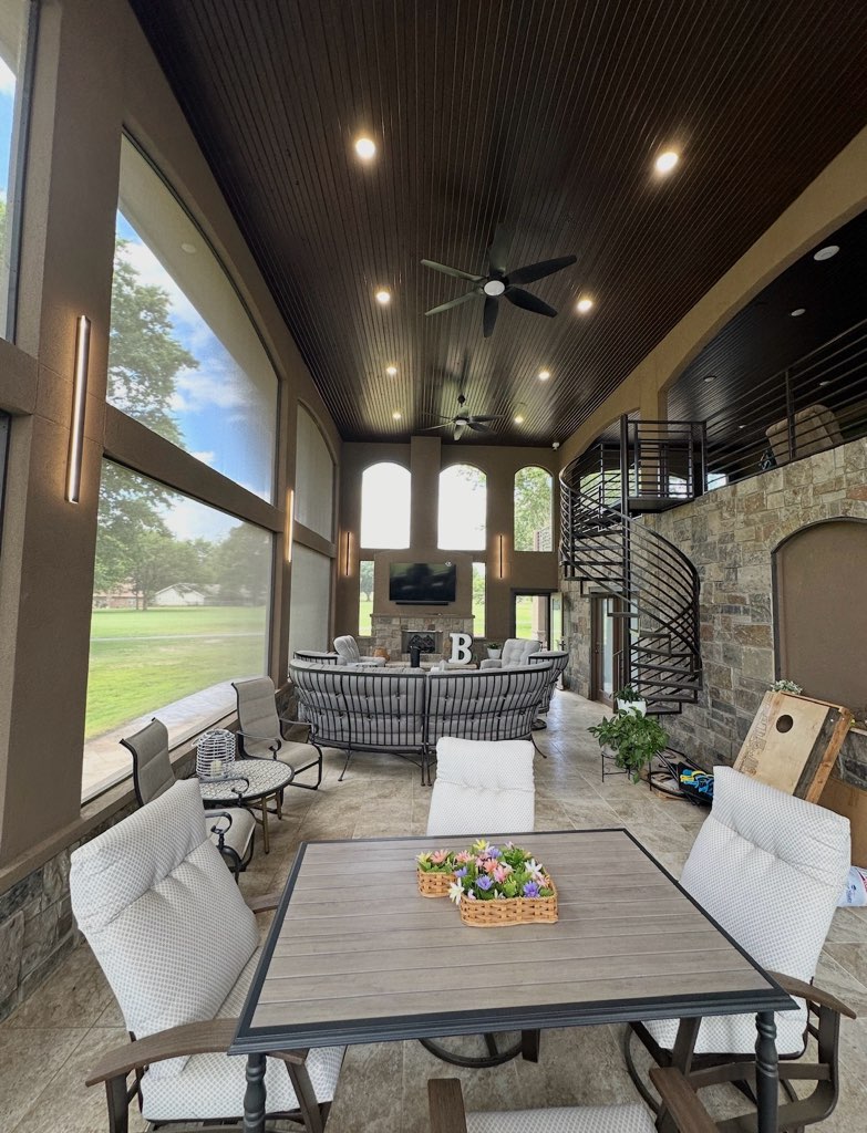 Covered patio with cushioned chairs, table, curved sofa, ceiling fans, and large screened windows